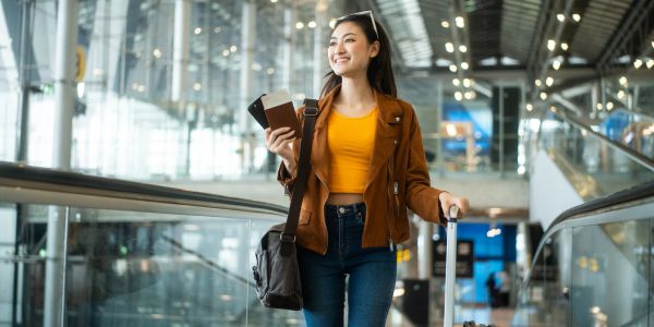 Young woman walking in an airport with luggage and passport.