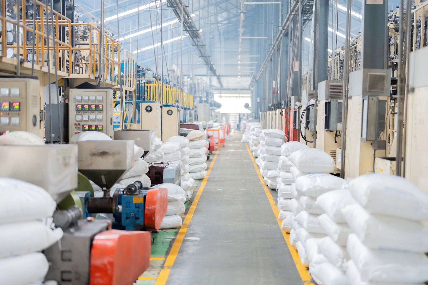 A clean industrial factory aisle lined with white bags and machinery on both sides.