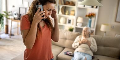 Worried woman talking on phone with elderly woman sitting on couch.