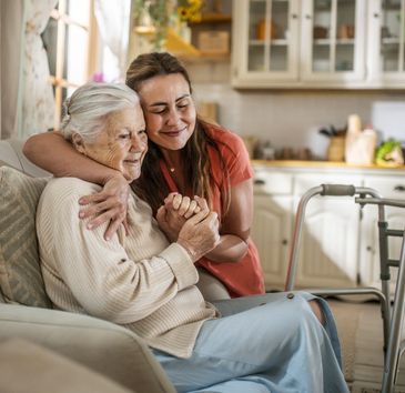 Young woman lovingly hugs elderly woman at home, showing care and support.