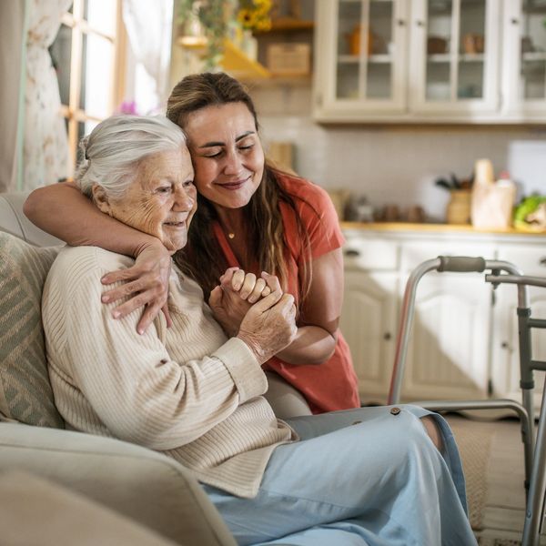 A young woman lovingly embraces an elderly woman sitting on a couch.