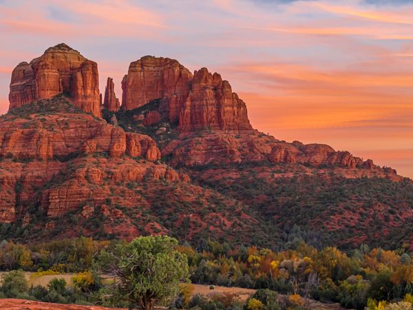 Sunset over red rock formations and green vegetation.