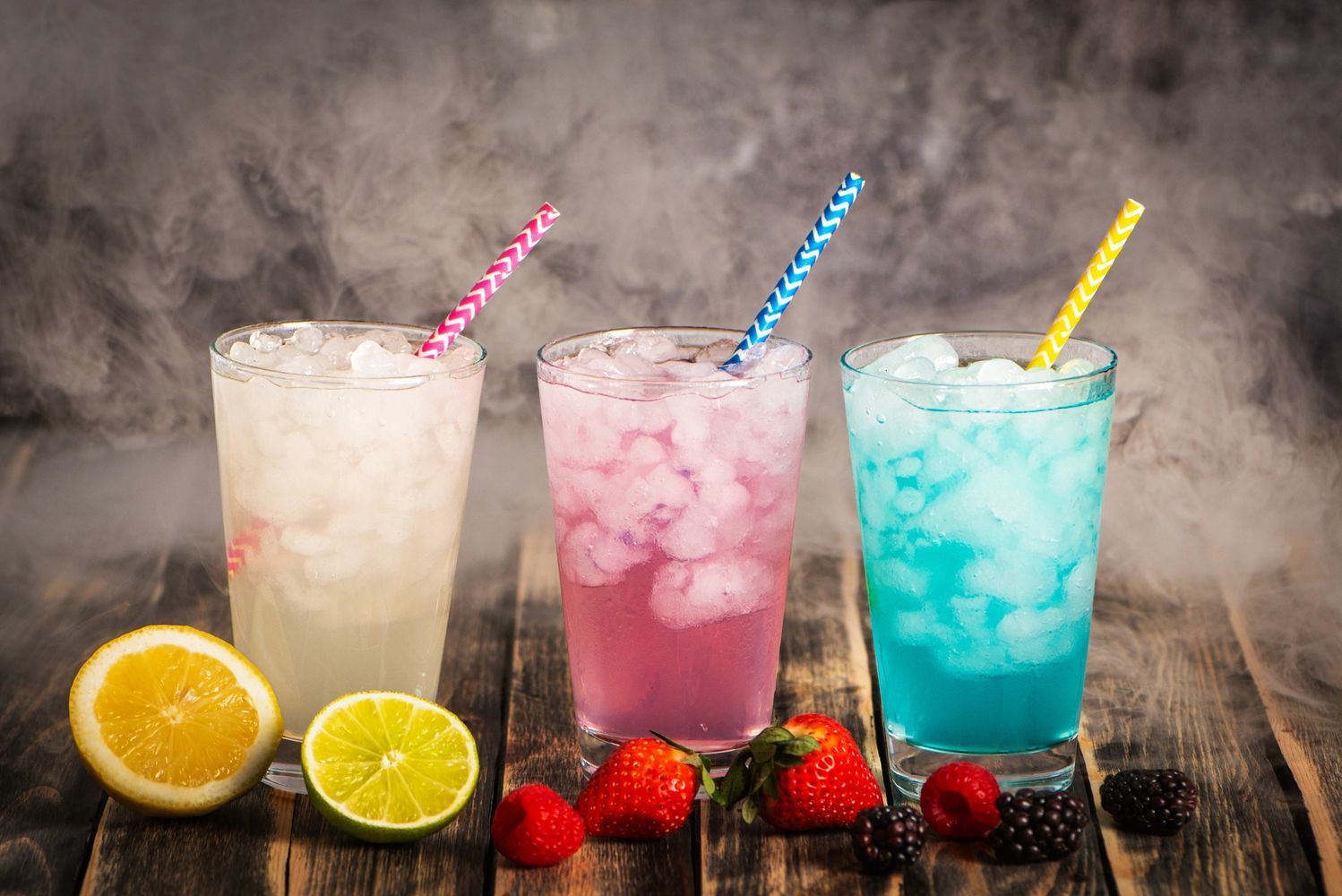 Three colorful iced drinks with fruit garnishes and striped straws. Sip Society Soda Bar providing a DIY dirty soda drink experience. 
