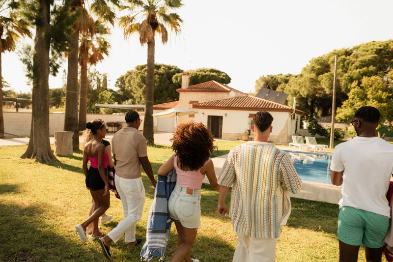 Group of friends walking towards the swimming pool at a luxury villa during their summer vacation