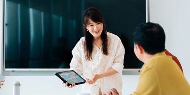 Woman showing tablet to people in meeting.