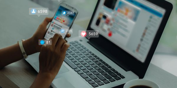 Person engaging with social media on phone and laptop, showing notifications.