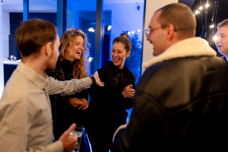 Individuals smiling and enjoying casual conversation in an indoor setting during an evening social event.