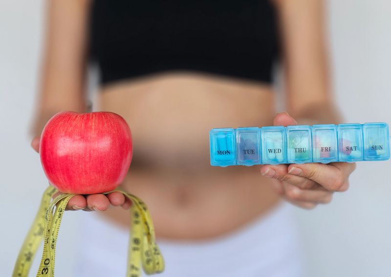 A person holds a red apple in one hand and a weekly medication organizer in the other, symbolizing the balance between healthy eating and medication management.
