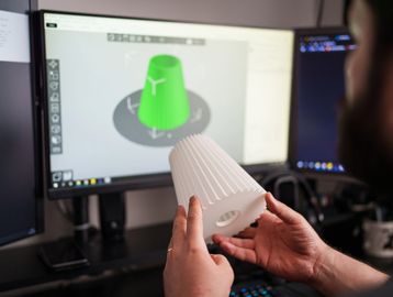 Person holding a 3D printed object matching the design on the computer screen.