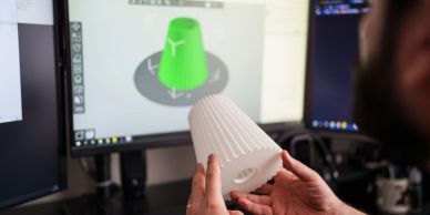 手持3D打印模型与电脑屏幕上的设计对比。