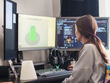 Person working on 3D modeling and coding at a multi-monitor setup.