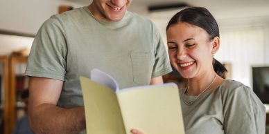 Two people smiling while reading a document together.