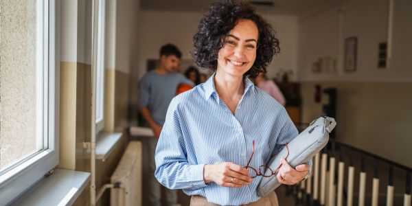 Smiling woman holding glasses and a tablet in a hallway.