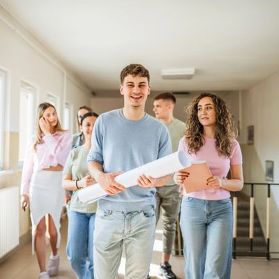 Group of young adults walking in a hallway, holding papers and a tablet.
