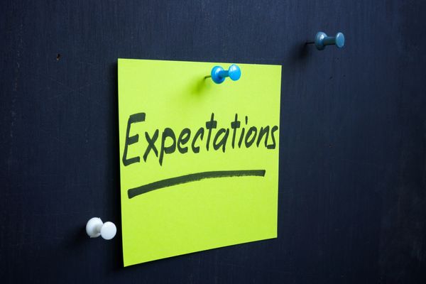 A bright green note pinned on a black surface with the word 'Expectations' written on it.