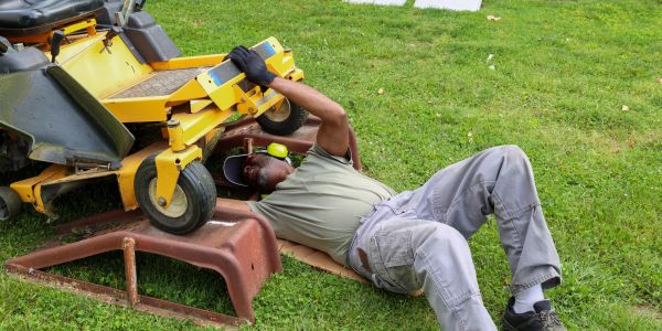 Man fixing a riding lawn mower on grass.