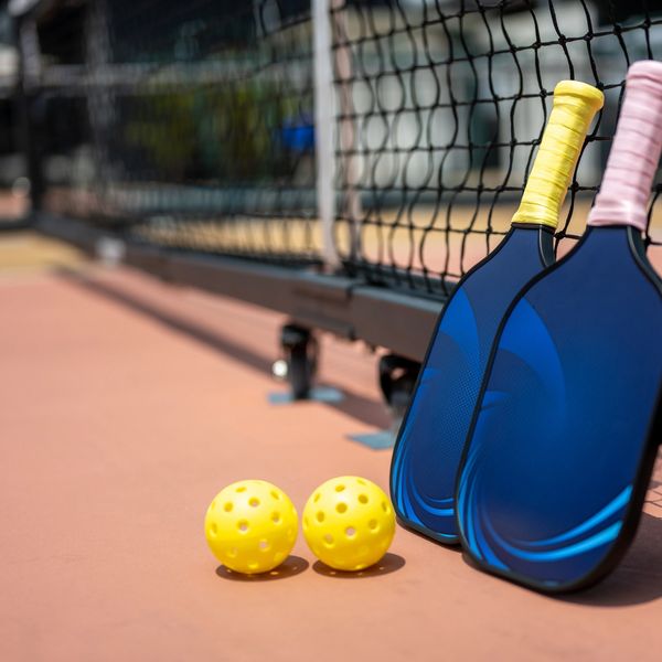 Two pickleball paddles and balls resting near a court net.