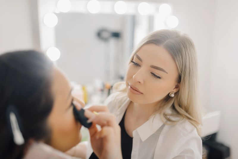 Professional makeup artist carefully applying eyeshadow on client's eyelid, creating a flawless look in a bright beauty salon