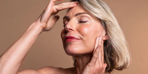 Mature woman gently touching her face with closed eyes, expressing calm and self-care.