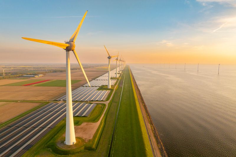 Rows of wind turbines and solar panels on the IJsselmeer shore and offshore wind turbines in the background in the Noordoostpolder in Flevoland, The Netherlands, during a springtime sunset seen from above.