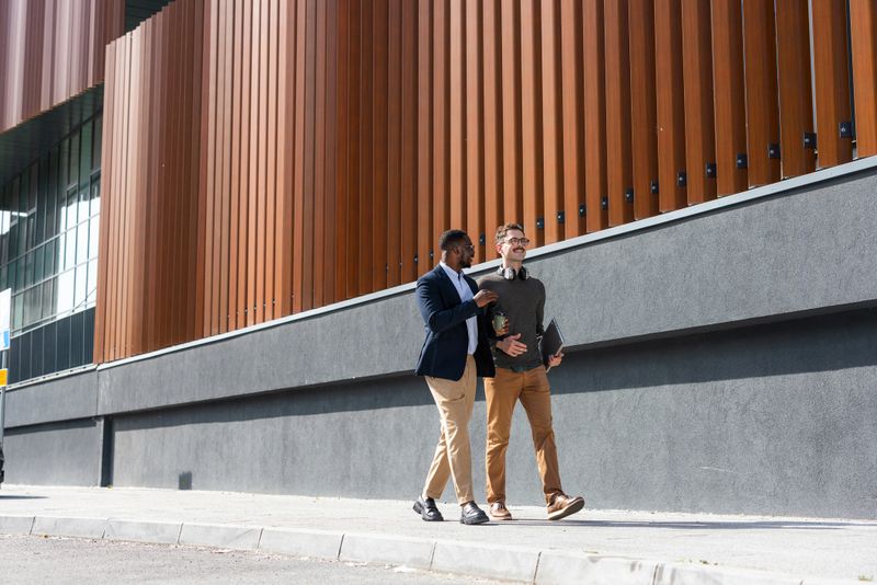 Two colleagues engaged in conversation while walking outdoors near a contemporary building facade.