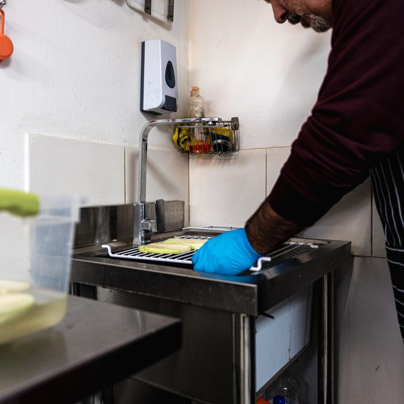 Mature man washing vegetables in kitchen sink – fresh food prep in small business setting