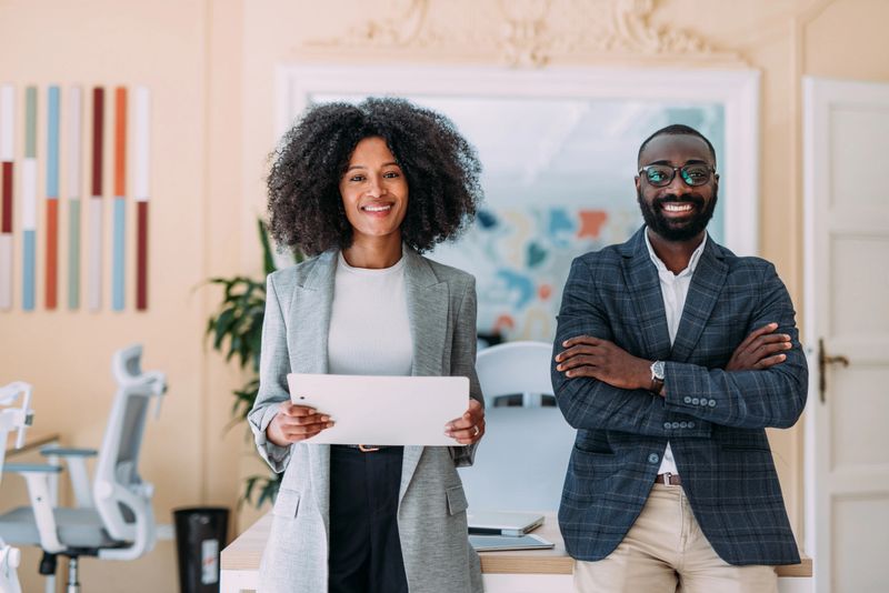 Shot of two confident business persons standing side by side with folded arms in the office and looking at camera. Portrait of successful businessman and businesswoman posing together in their office.