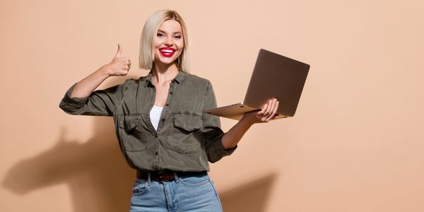 Smiling woman holding a laptop and giving a thumbs-up gesture.