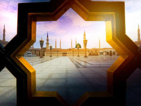 View of a mosque courtyard framed by a star-shaped window at sunset.