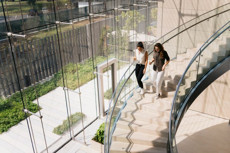 Two businesswomen walking and talking on stairs in modern office building