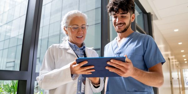 Two healthcare professionals reviewing information on a tablet in a hospital corridor.