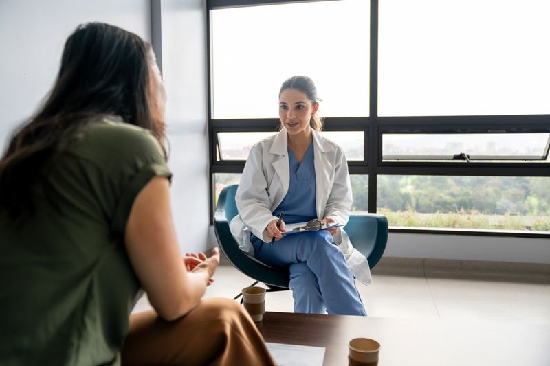 Latin American female doctor talking to a patient in a consultation at the hospital while taking notes on a clipboard