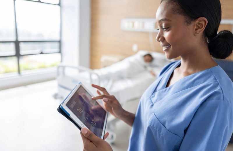 African American pediatric nurse monitoring the vital signs of a patient in a digital tablet and smiling