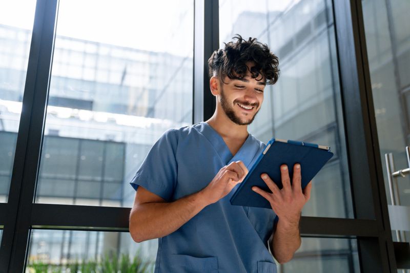 Portrait of a happy Latin American male nurse working at the hospital using a digital tablet and smiling - healthcare occupation concepts
