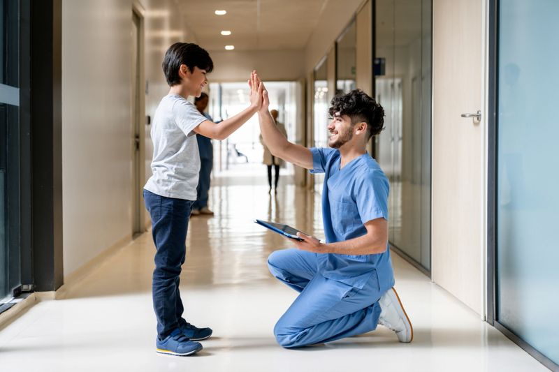Happy Latin American nurse giving a high-five to a boy at the hospital and smiling - pediatric medicine concepts