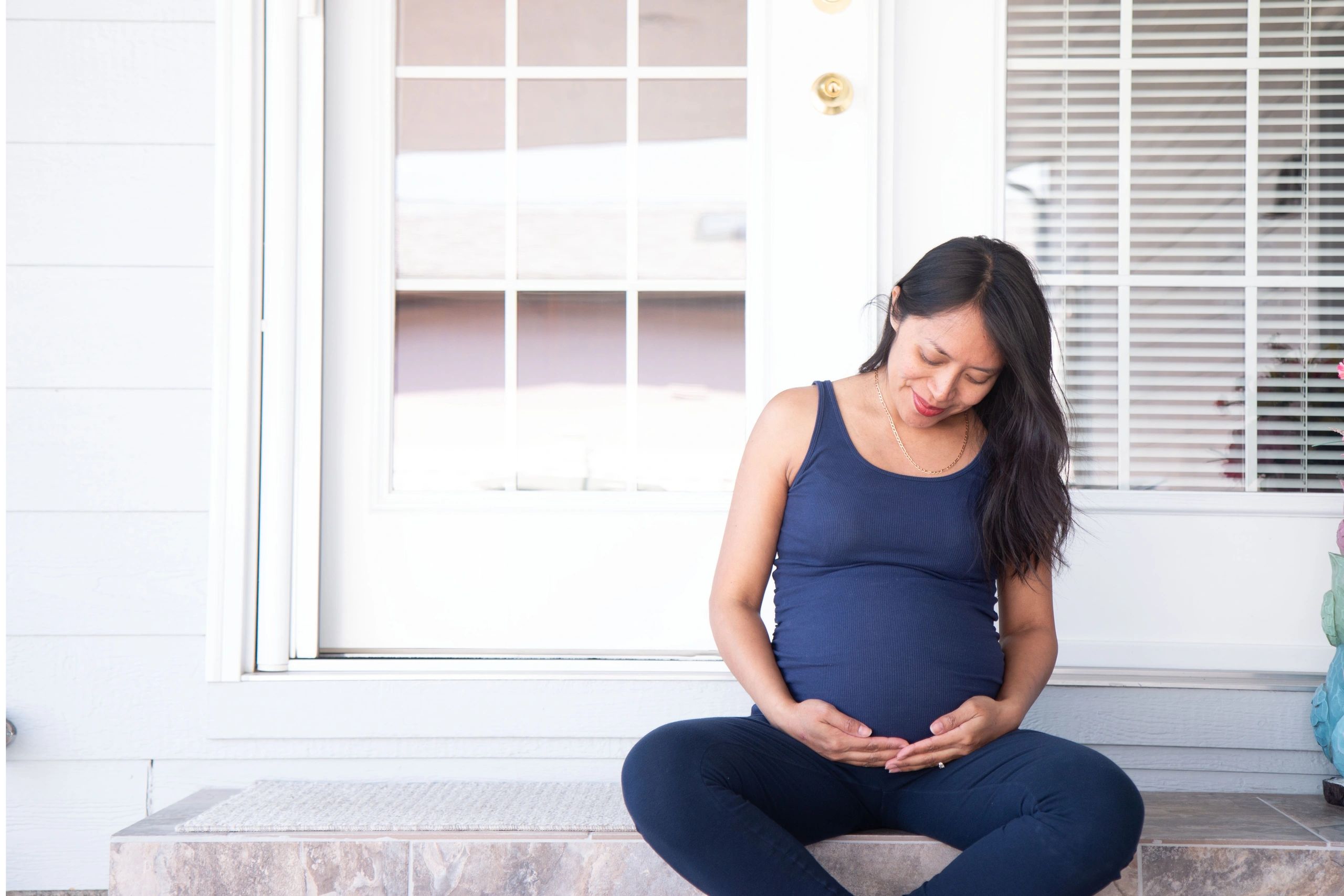 Pregnant woman sitting on porch, smiling at belly.