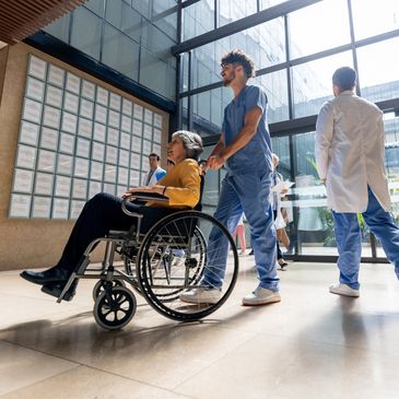 A nurse pushes a patient in a wheelchair through a hospital lobby.
