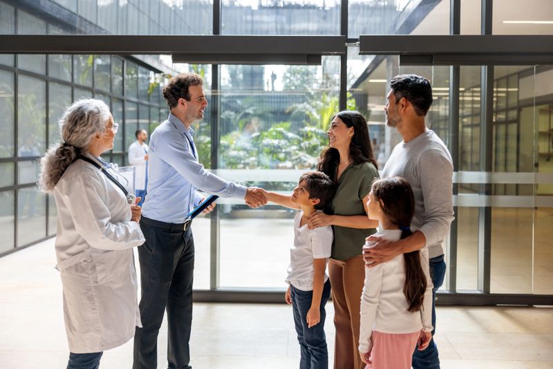 Happy Latin American family at the hospital greeting a health insurance agent with a handshake in front of their doctor