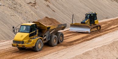 Heavy construction machinery working on a sandy dirt road.