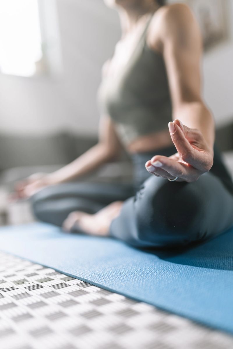 A person is engaged in yoga, seated on a blue mat with crossed legs in a calm indoor environment. They focus on mindfulness, surrounded by soft lighting and a peaceful atmosphere.