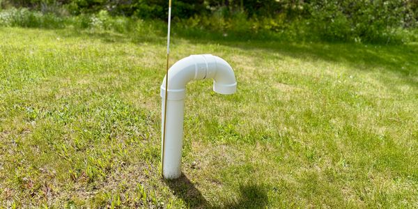 White PVC pipe sticking out of grassy field with a measuring rod beside it.