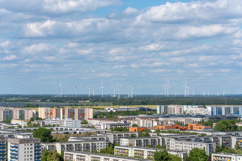 An urban residential area stretches to the horizon, where numerous wind turbines generate energy. Modern urbanity meets sustainable technology.