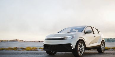 Sleek white electric SUV parked on a rugged terrain during sunset.