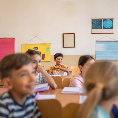 Happy boy sitting in classroom surrounded by other students.