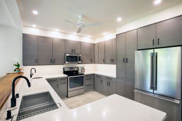 Modern kitchen with gray cabinets, stainless steel appliances, and white countertops.