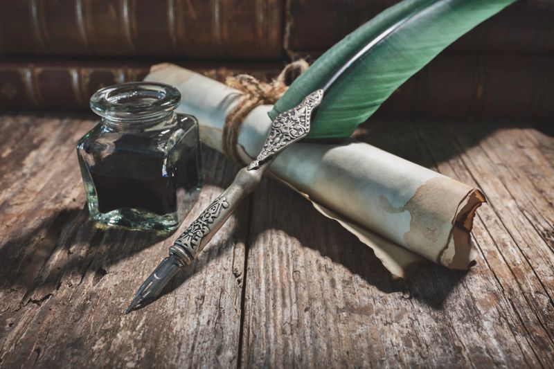 Quill pen with green feather, ink well and scroll parchment paper on desk with books