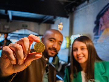 A man holding a gold coin with a woman smiling beside him indoors.