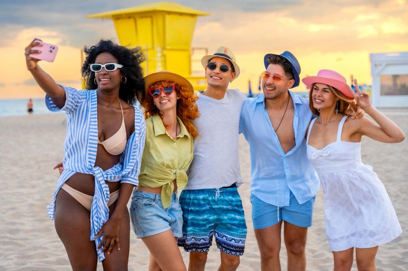 Group of cheerful young friends enjoying a sunny beach day, capturing joyful memories with a selfie during their summer vacation