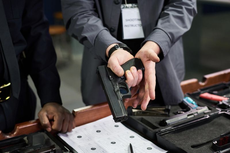 Close-up shot showing instructor guiding individual on proper handgun handling technique during firearm safety training in an indoor range environment