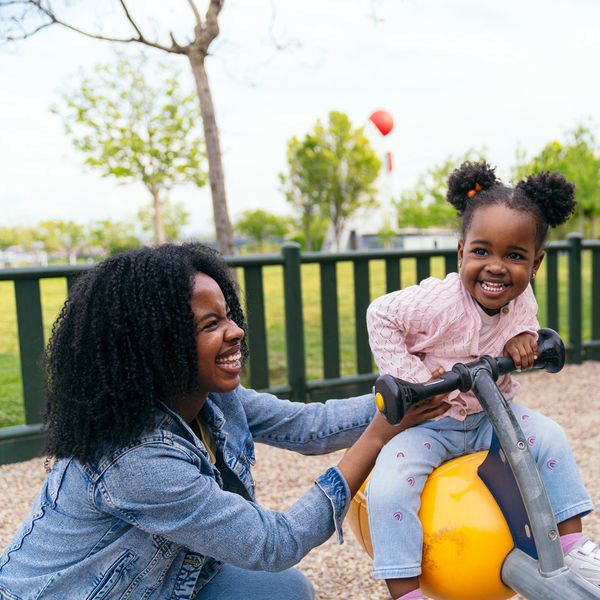 A joyful mother helps her smiling daughter on a playground ride.